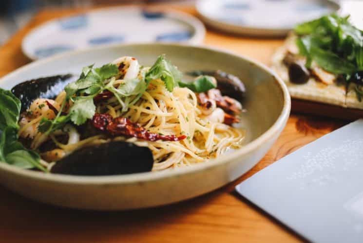 Oval bowl filled with spaghetti noodles, red peppers, clams and greens