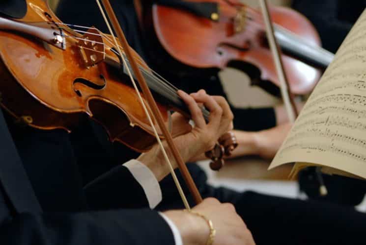 Two violinists in dark suits playing with open sheet music