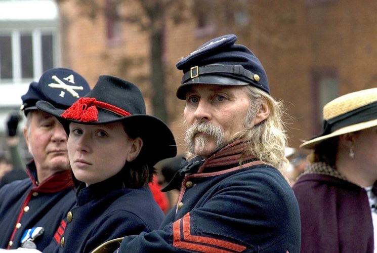 Two men and a woman standing outside in dark blue and red Civil War period costumes