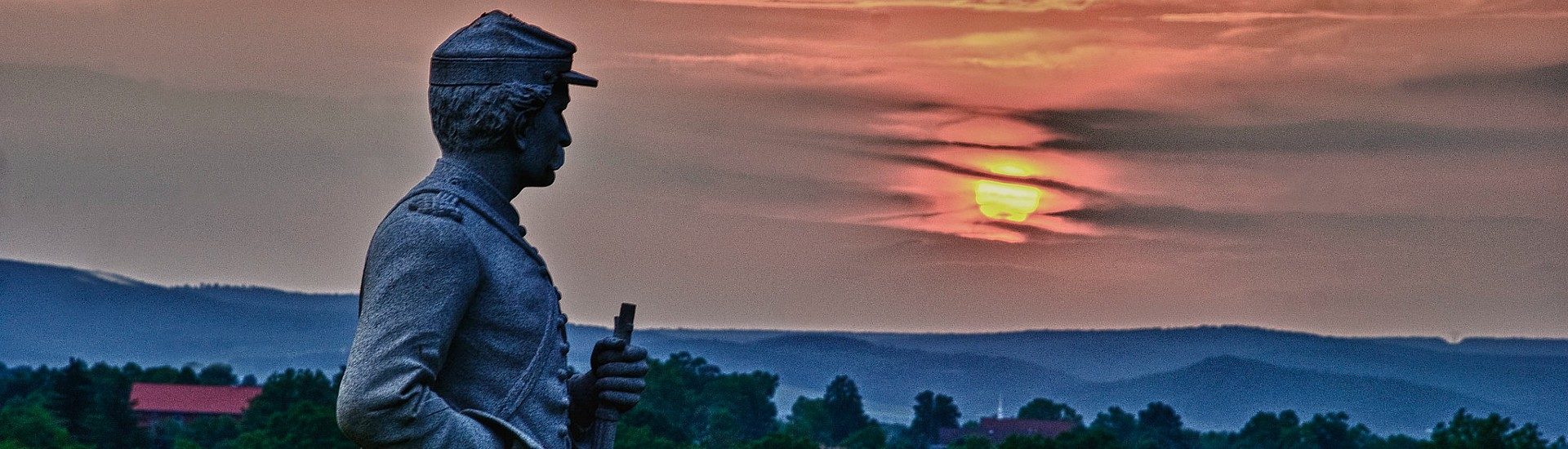 Statue of a soldier overlooking an expansive sunset sky with a hilly mountain range