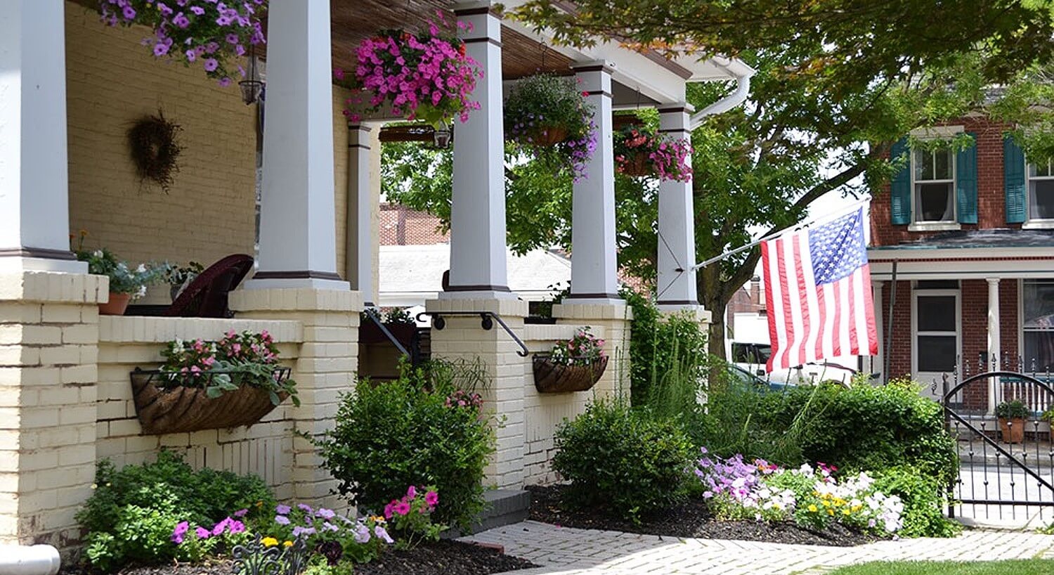 Front porch of a brick home with tall white pillars, beautiful hanging baskets and flag on a pole