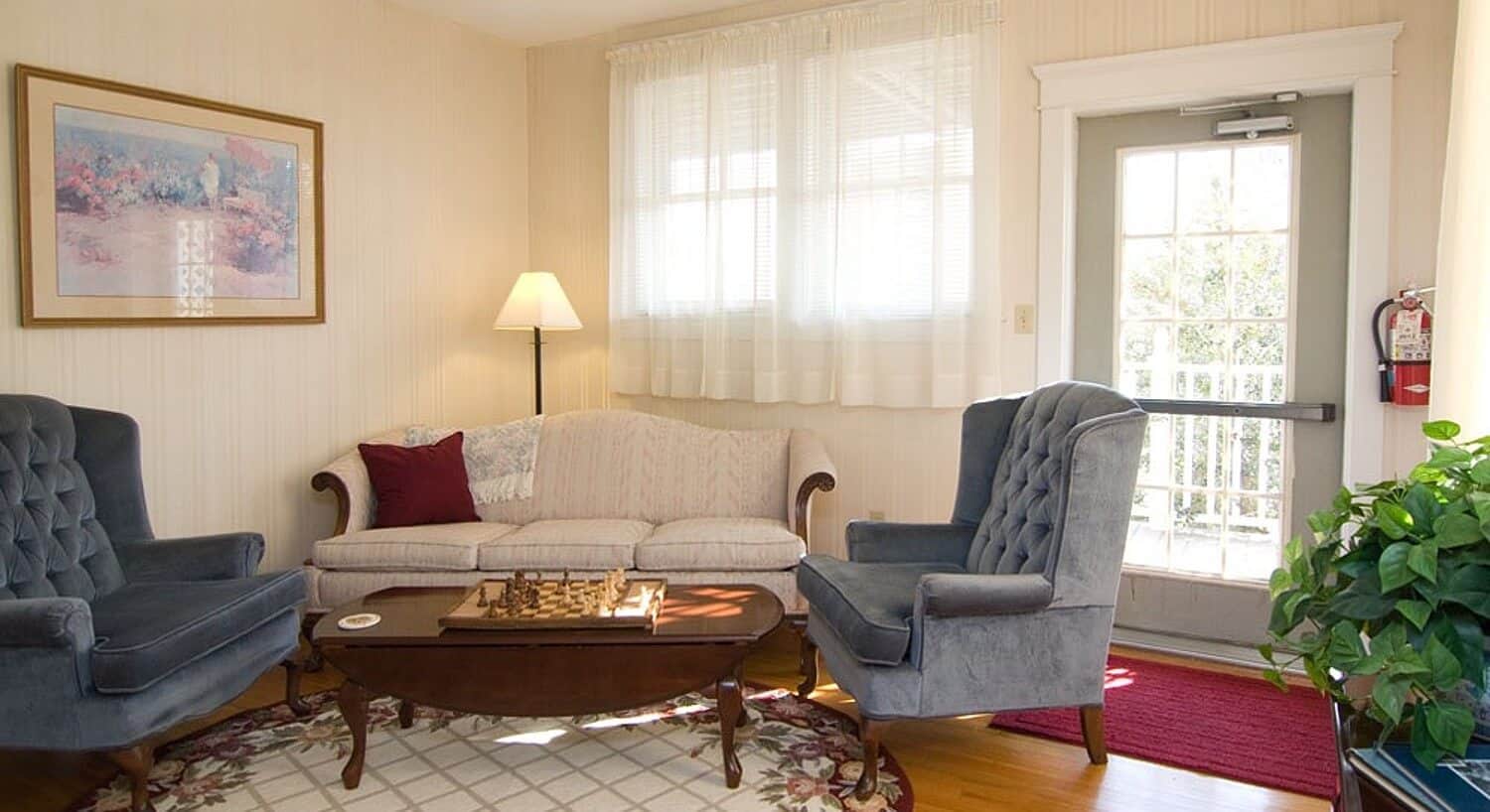 Elegant sitting room with couch, two wingback chairs, coffee table and door to the outdoors