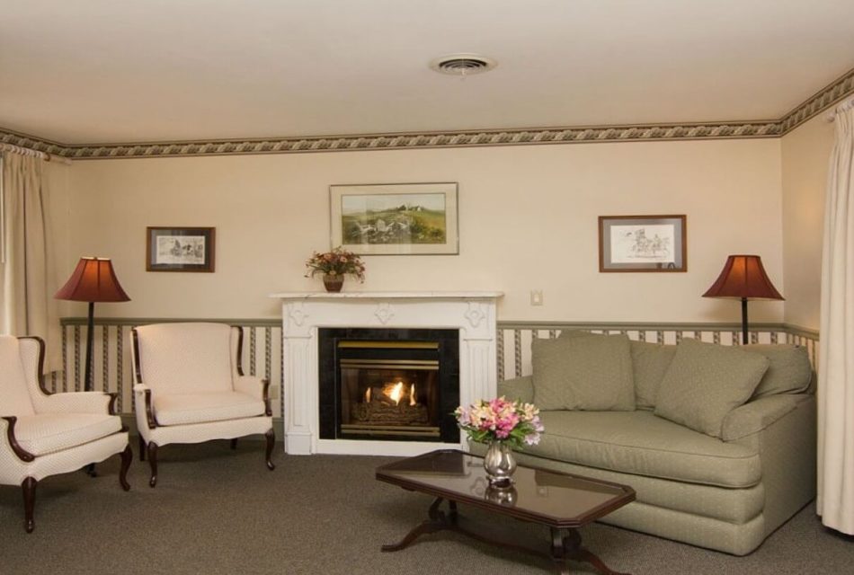 Siting area of a bedroom with gas fireplace, loveseat and two white chairs
