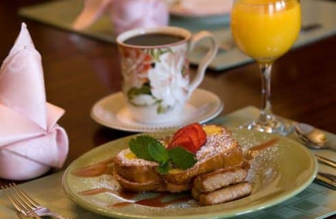 Breakfast plate with French toast, sausage, and strawberries with coffee and orange juice