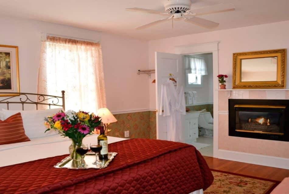 Large bedroom with king bed, gas fireplace and door open to a bathroom with two white hanging robes