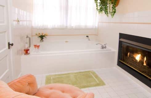 White bathroom with large jacuzzi tub, gas fireplace and tuffed sitting chair