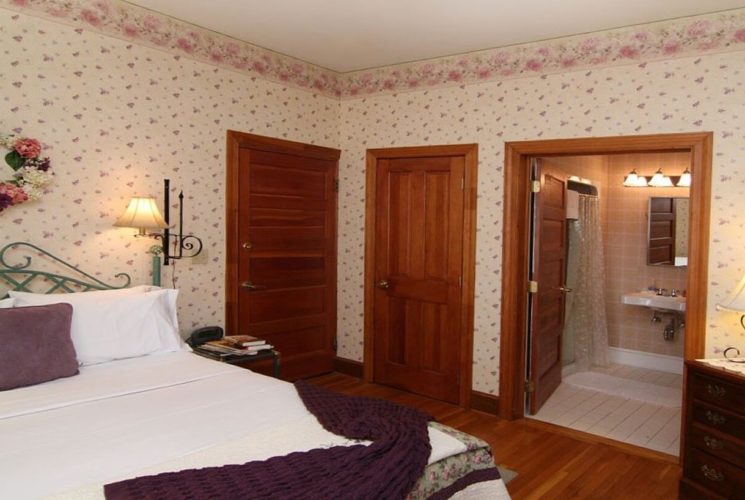 Guestroom with queen bed, dresser with lamp, and doorway open into bathroom