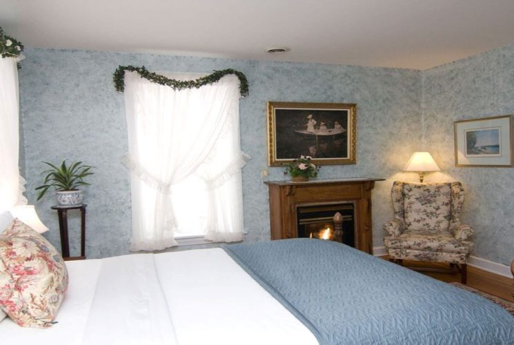 Guestroom with queen bed, gas fireplace, sitting chair and bright windows