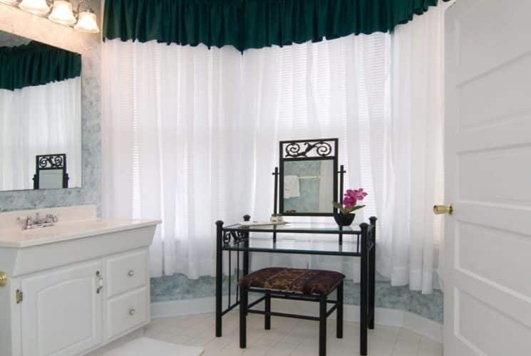 Bathroom with large bay window, glass table with mirror and bench and single sink vanity