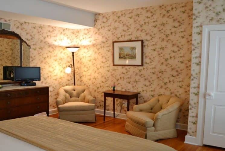 Sitting area of a bedroom with two club chairs, tall lamp and dresser with mirror