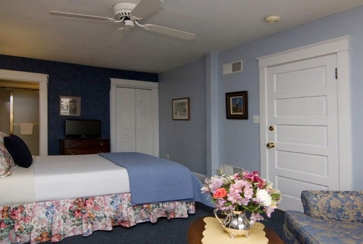 Bedroom with blue walls, queen bed with floral bedskirt and blue flowered couch