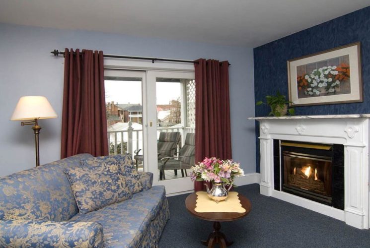 Sitting area of a bedroom with couch, table, gas fireplace and slider door to patio