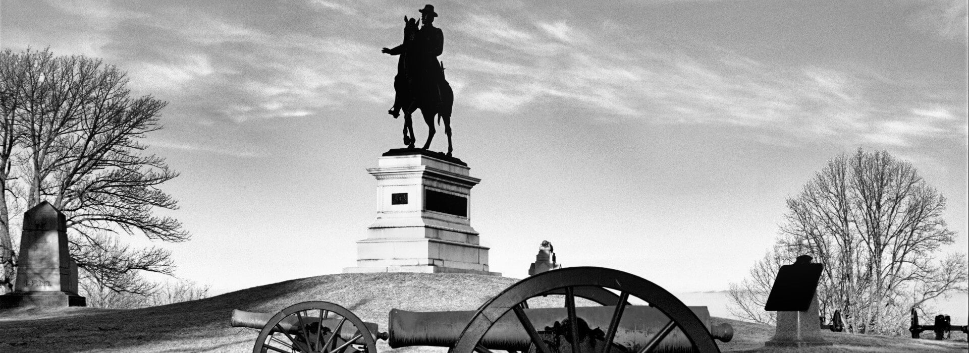 Large statue of a man on a horse on top of a small hill with a cannon in front