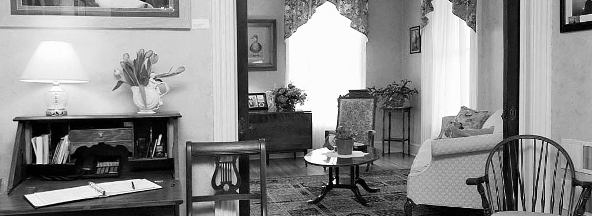 Parlor room of a home wth couch, table, sitting chairs and writer's desk