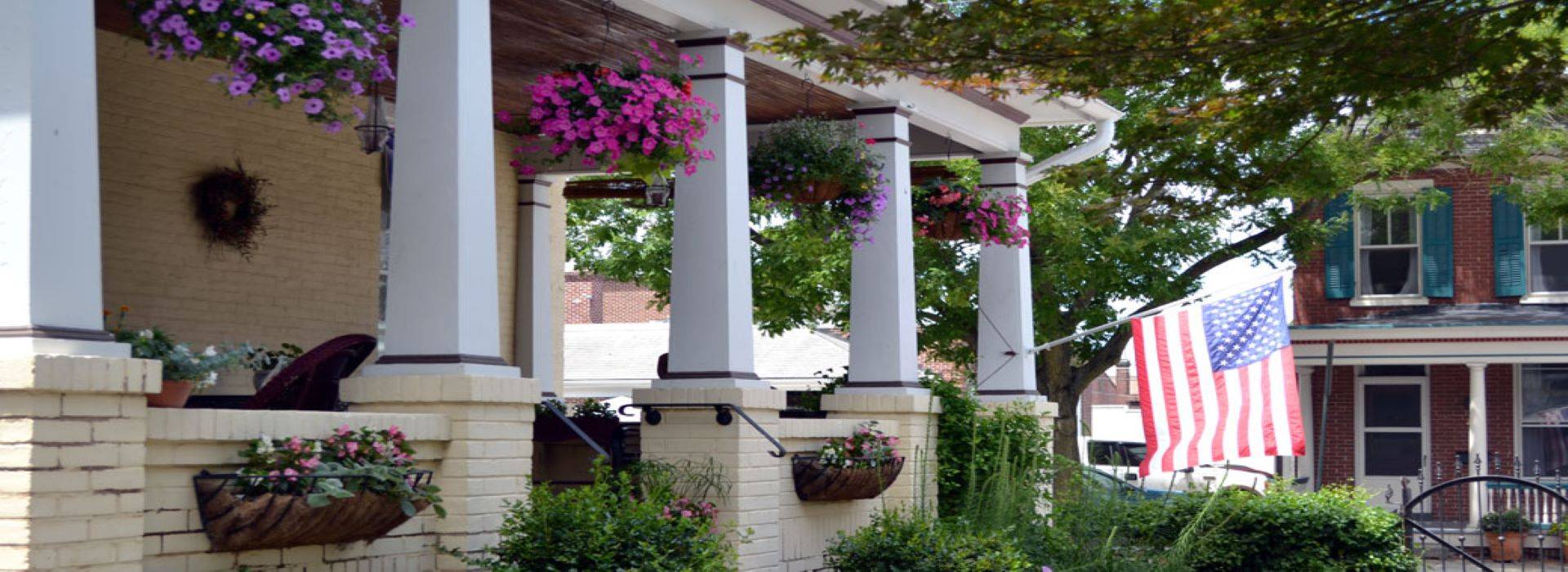 Front patio of a home with tall white columns, hanging flower baskets and a flag