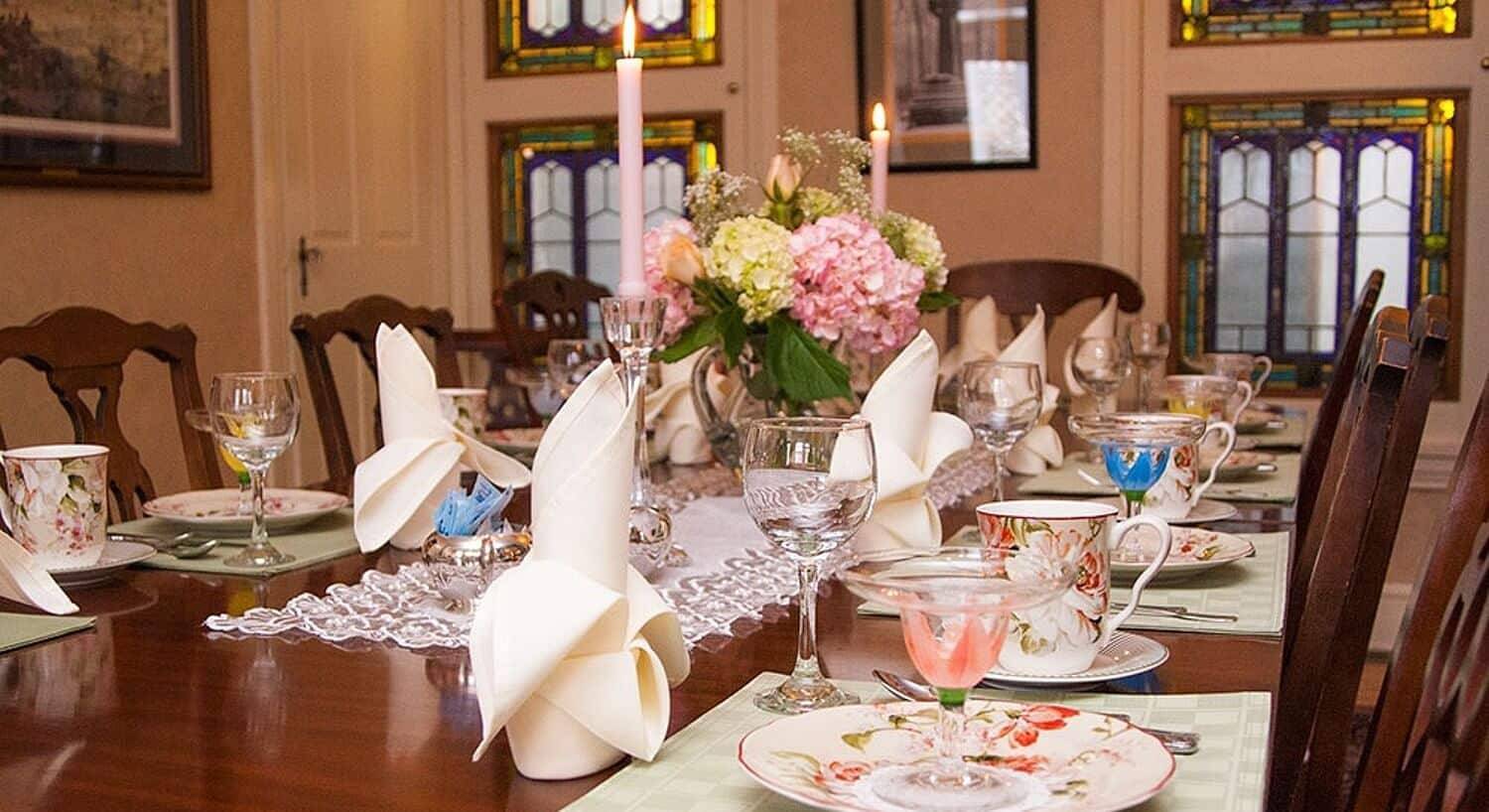 Elegant dining table set with floral china, folded napkins, candles and vase with flowers