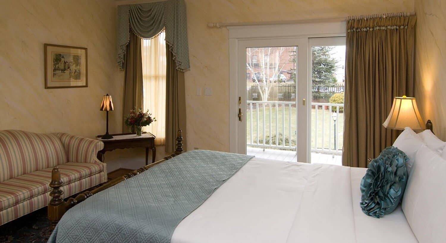 Bright guestroom with queen bed, striped couch and large slider door onto outdoor patio