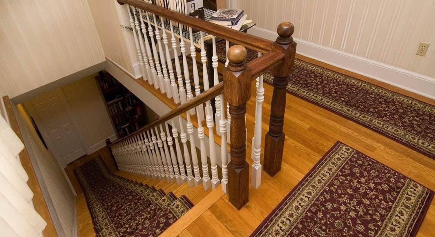 Upstairs hallway of a home with rugs on hardwood floors and long stairwell leading downstairs