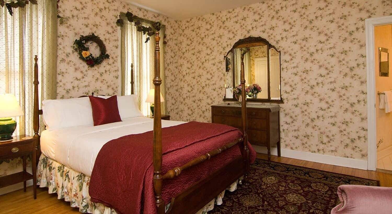 Guestroom with queen four poster bed, flowered wallpaper and oriental rug