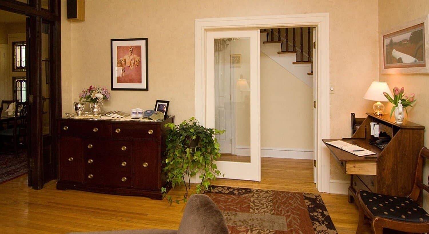 Foyer of a home with dresser, writing desk and French doors opening to a hallway with a staircase