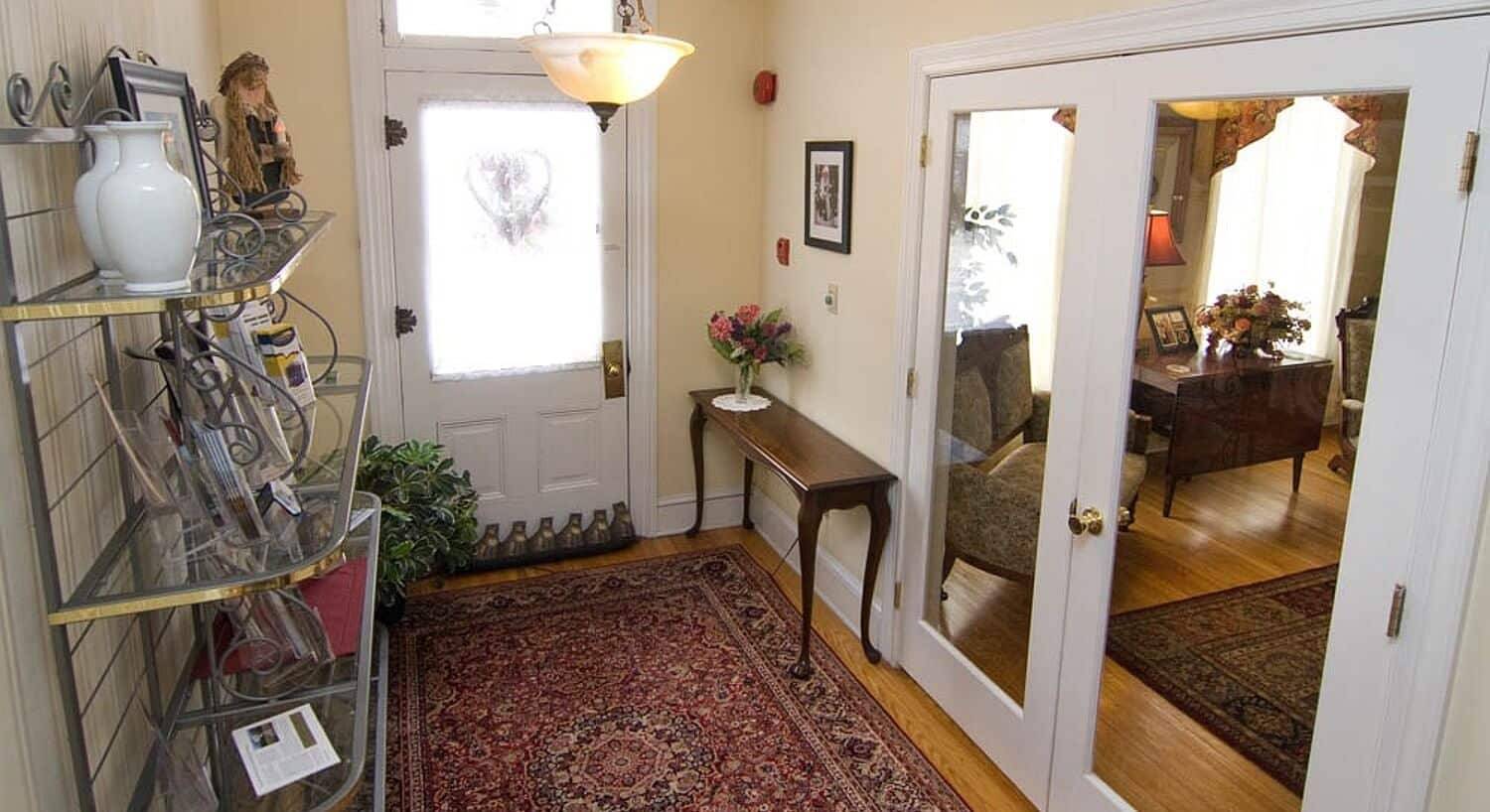 Front entry of a home with tall metal shelving unit, oriental rug and French doors looking into adjoining room