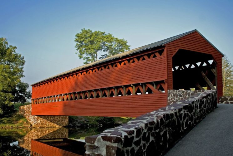 Large, red covered bridge with drive flanked by stone wall