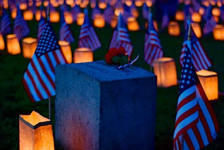 Single headstone surrounded by American flags and lit paper lanterns