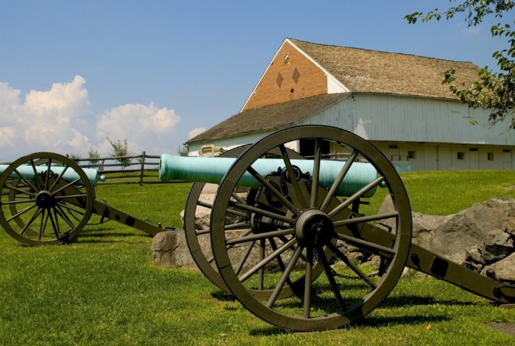 Two antique cannons in a large green field with a white barn